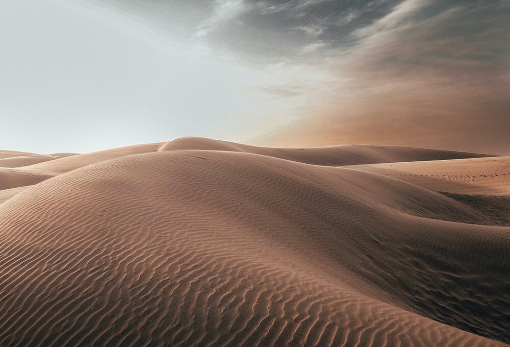 Majestic sand dunes under a dramatic sky, capturing the serenity of the desert at dawn.