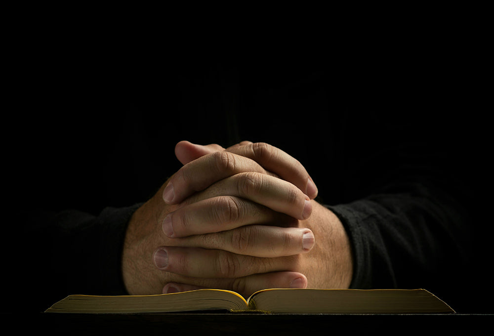 Hands clasped in prayer on a bible