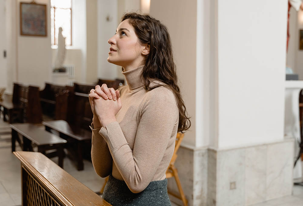 Woman praying beside an open Bible and journal during quiet time with God.