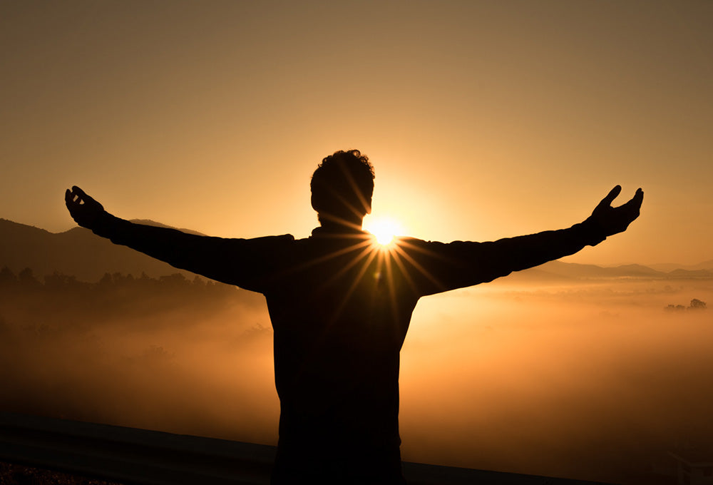 Man looking over a canyon at sunset with his arms open wide encouraging the pursuit of His presence