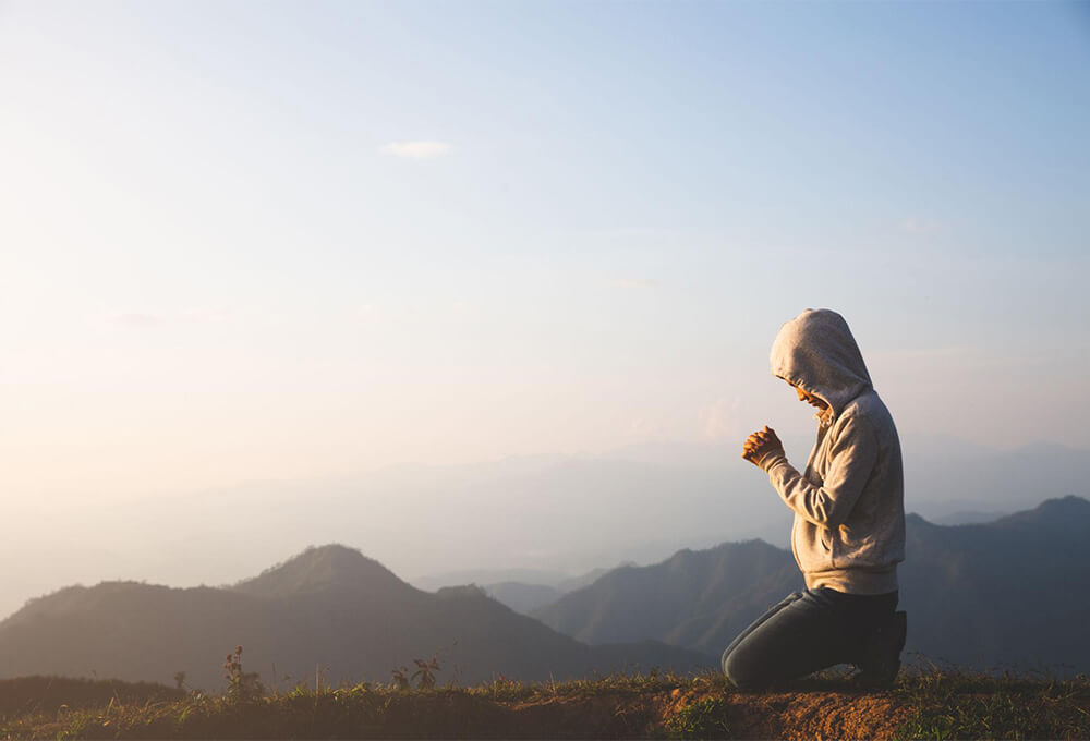 Woman kneeling in prayer at the top of a mountain