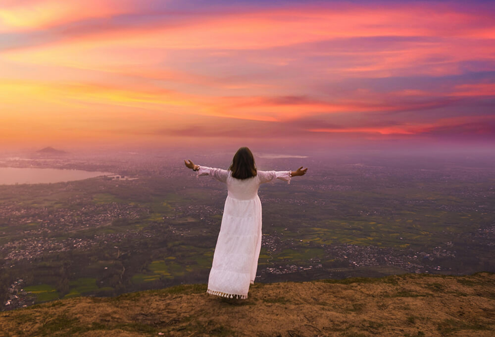 woman standing on a hill at sunset with arms outstretched reflecting peace and spiritual surrender