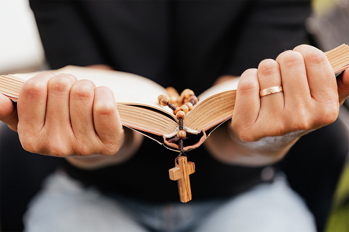 A woman praying beside an open Bible in soft natural light.