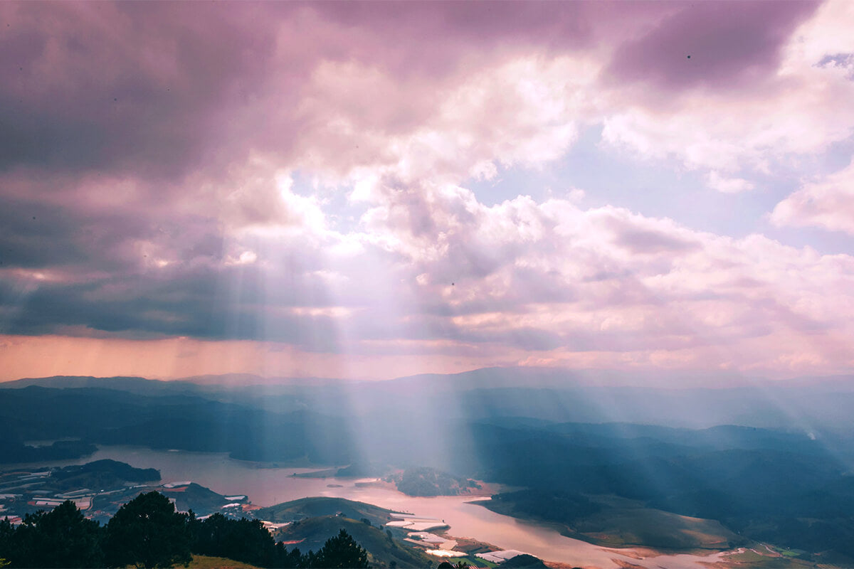 Sunlight breaking through dark clouds over a peaceful landscape, symbolizing hope and courage through faith.