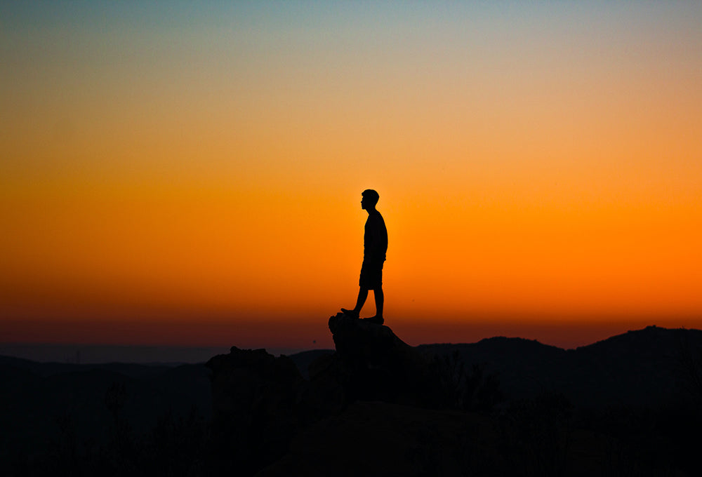 man on a rock at dusk looking into a yellow beautiful sky thinking about God's love