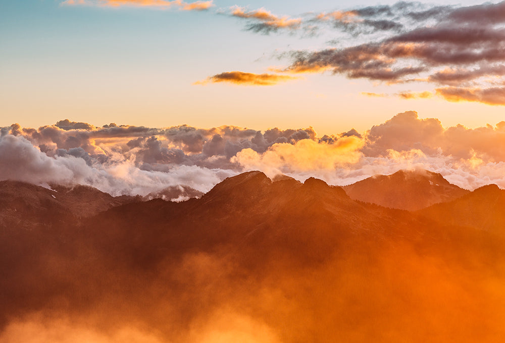 Dreamy image of flying over mountains at sunrise with orange glow across the clouds