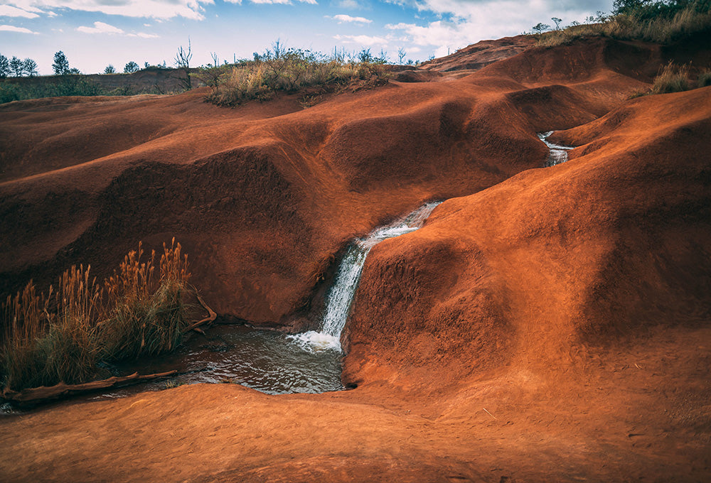 Scene of a stream running through lush tan hills 