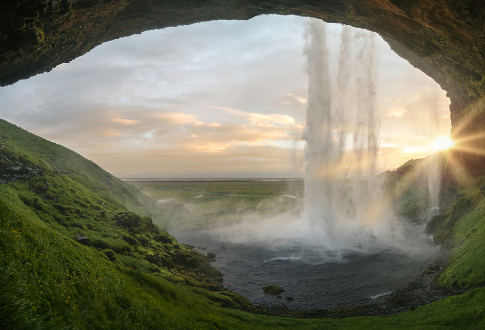 Waterfall and a lush cave with the sun rising over the hills