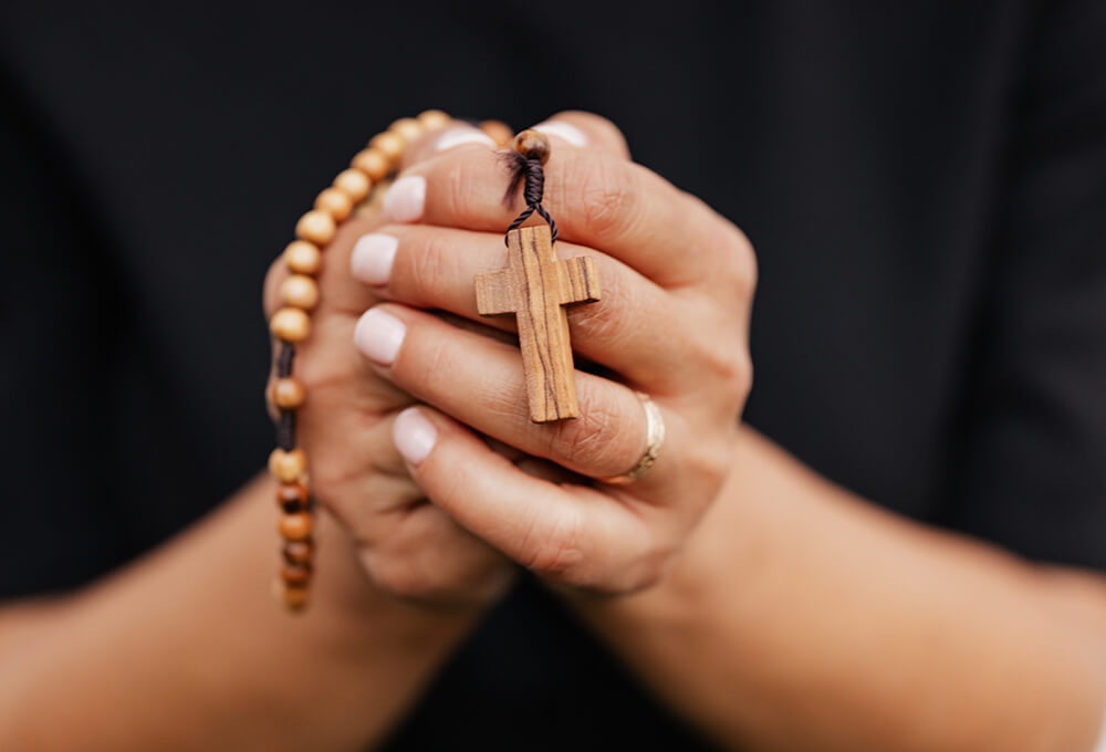 hands clasping a wooden rosary with cross