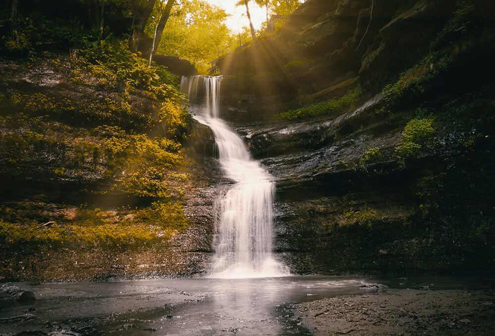 Beautiful waterfall flows into a secluded pond as the sun breaks through the trees