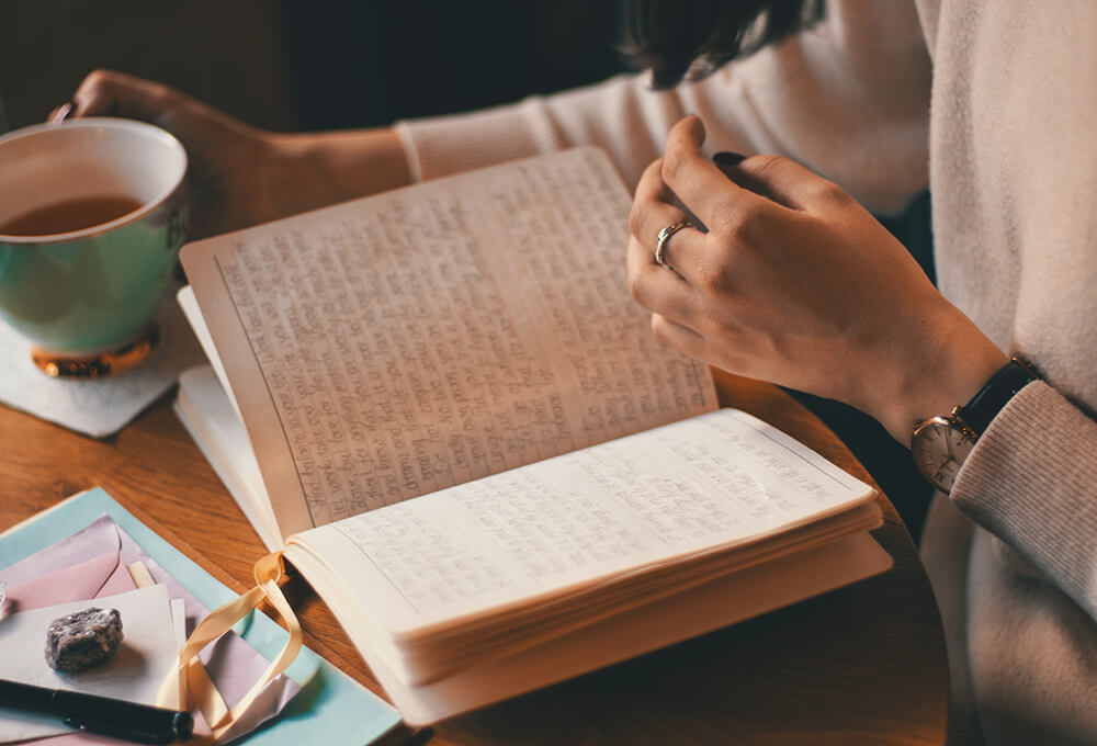 Woman drinking coffee while writing in her journal
