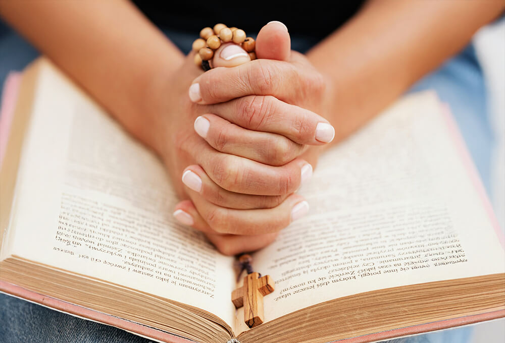 womans hands rested in prayer on an open Bible praying for spiritual growth