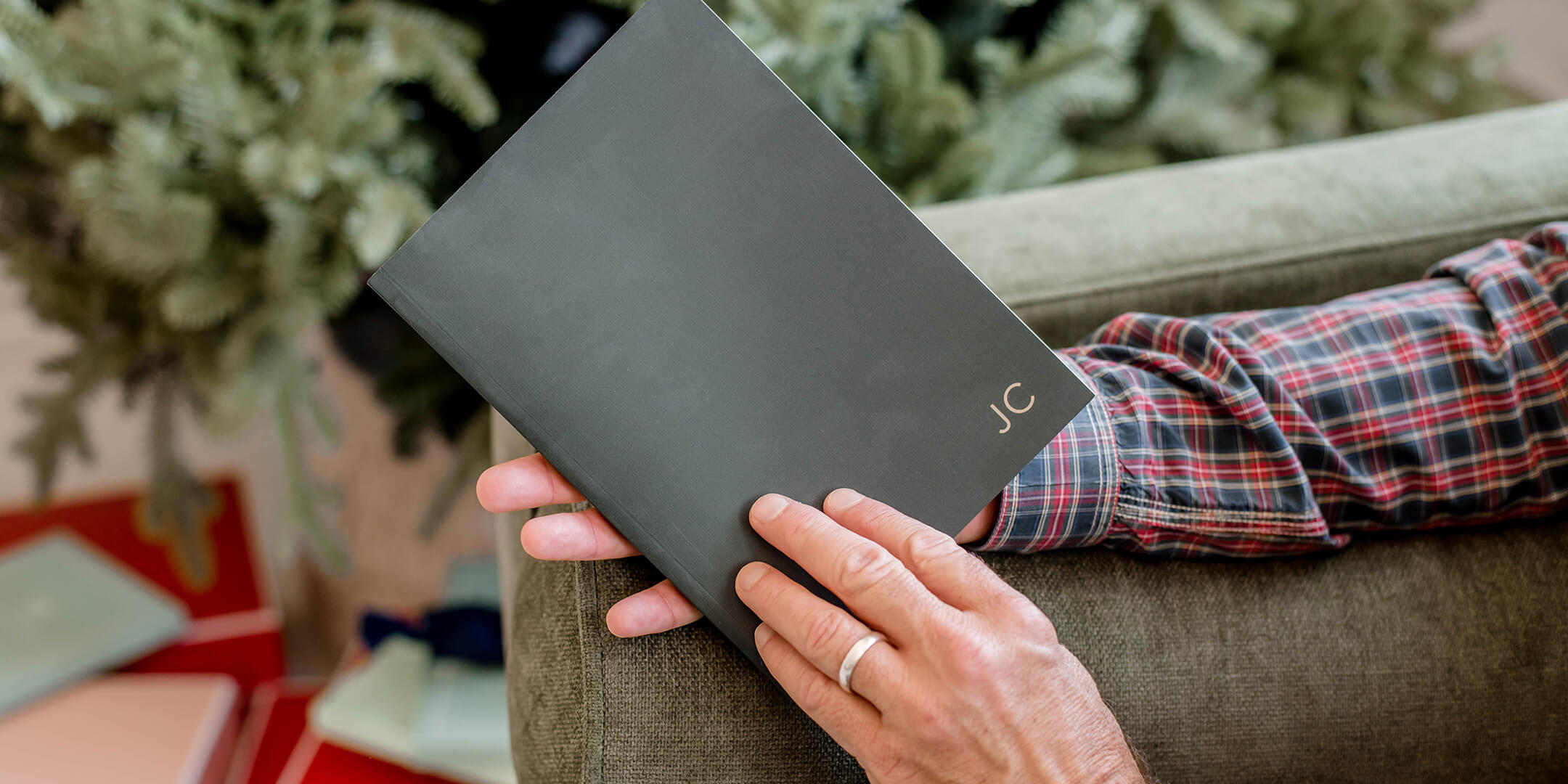 Man holding a beautiful green scripture journal in his hand sitting in a green chair with a tree in the background