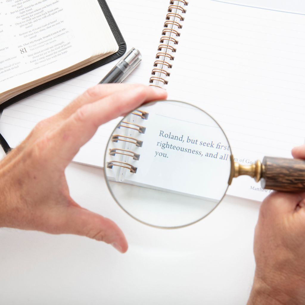 image of a man holding a magnifying glass looking at personalized scripture with a Bible on the side