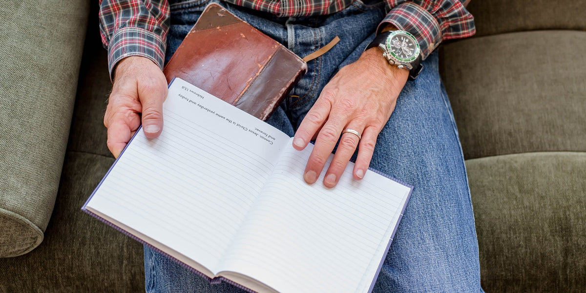 Man sitting down in jeans with a christian journal and Bible in his lap