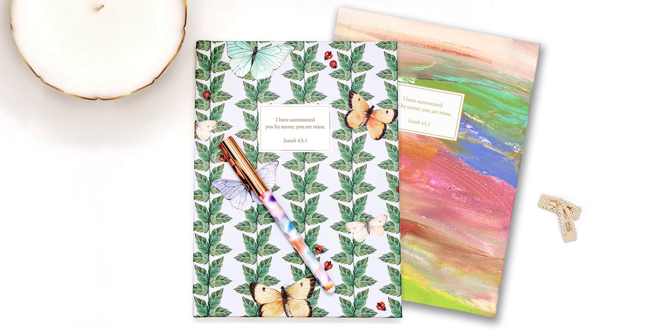 Two artist-designed personalized scripture journals by Paper Sunday styled with a candle and pen, creating a peaceful journaling setup with a unique curated set of Bible verses for daily reflection