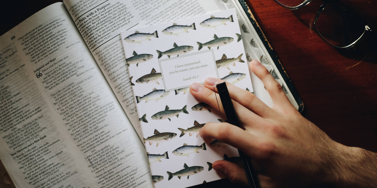 Man holding his scripture journal on top of a Bible with a pen in his hand