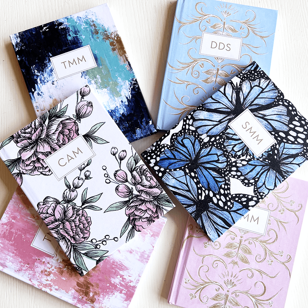 Theresa Mangum designed personalized scripture journals laid our on a white desk with flowers and butterflies
