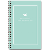 A planner with a light teal cover featuring a white frame and a butterfly design, with personalized scripture verse printed on it.
