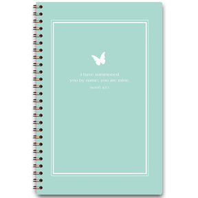 A planner with a light teal cover featuring a white frame and a butterfly design, with personalized scripture verse printed on it.