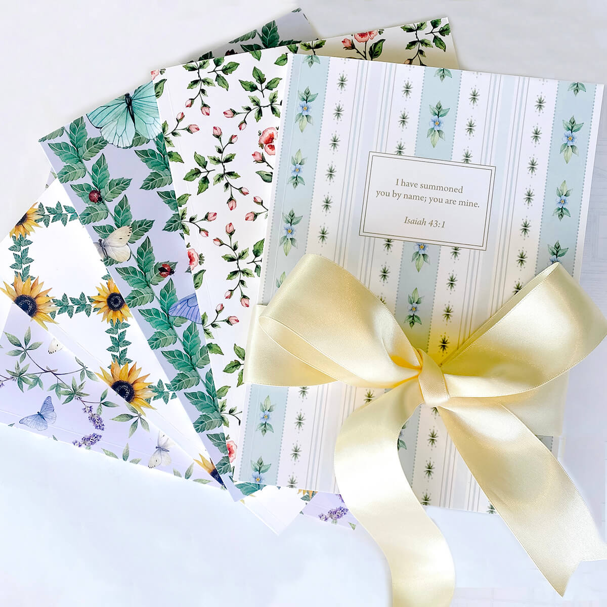 Collection of artist-designed personalized scripture journals by Paper Sunday styled with a yellow bow, including designs by Lydia Carraway, showcasing unique curated Bible verse journals for meaningful gifting