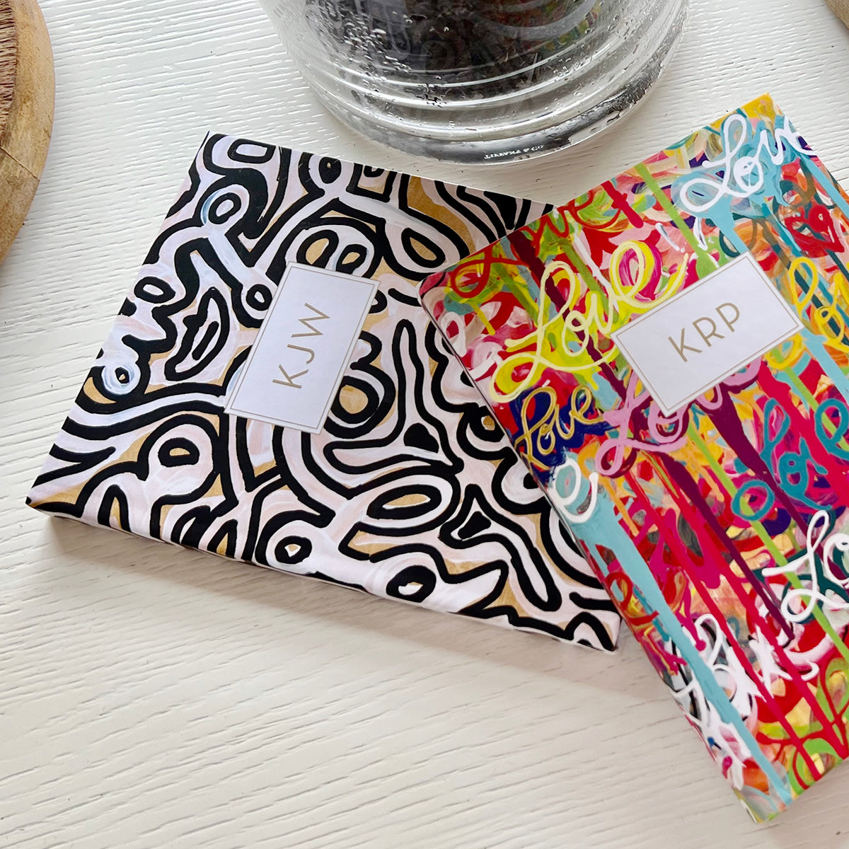 Custom planner with Love Is in the Air and Can't stop designs by Allison Castillo and personalized name on soft cover sitting on a white wood table with the bottom of a glass vase 