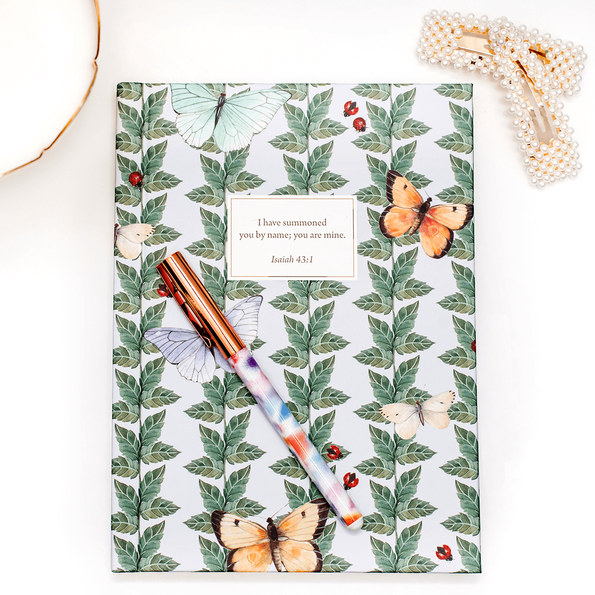 Hardcover Butterfly personalized scripture journal by Lydia Carraway styled with a decorative pen and hairclip, showcasing an elegant journaling setup with a unique curated set of Bible verses
