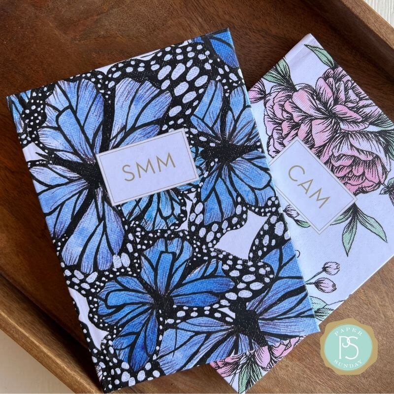 Monarch and Bouquet personalized scripture journals by Theresa Mangum stacked on a wood table, showcasing butterfly and floral designs with a unique curated set of Bible verses for reflection and gifting
